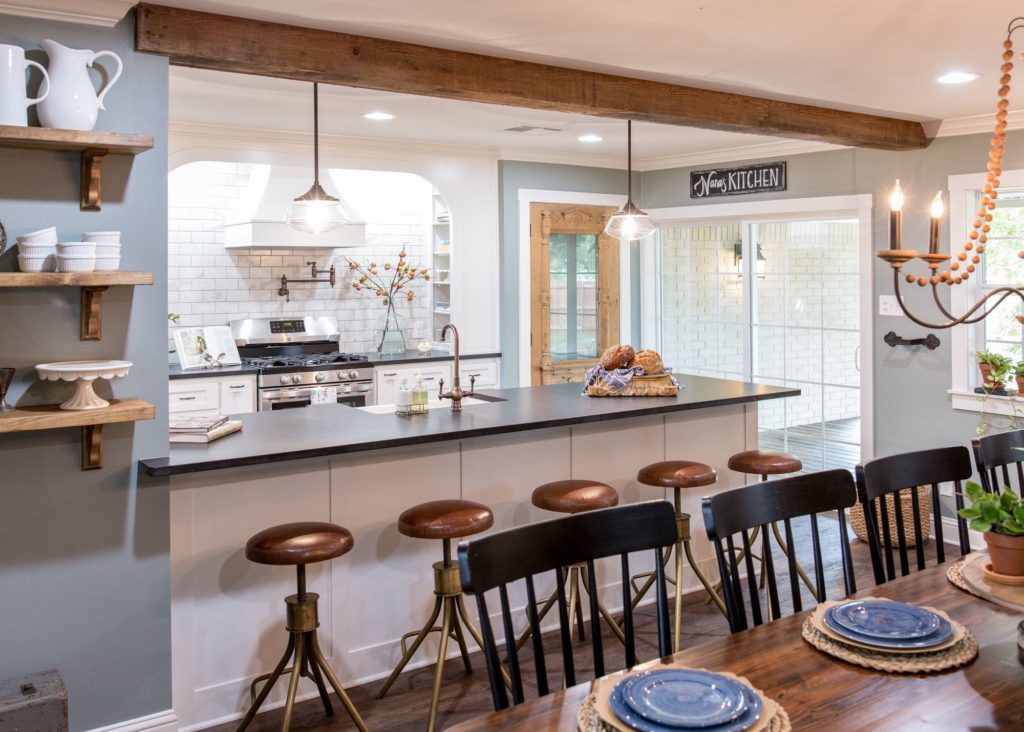 Fixer Upper Kitchen in The Mexia Manor House with white cabinets and back-splash along with a wood stained beam and doors that warm up the space www.PattersonDecoratingGroup.com/blog
